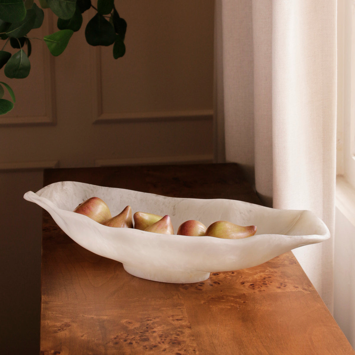 White resin bowl with fruits on a wooden surface near a window