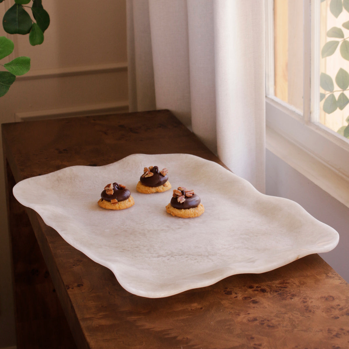Three cookies with chocolate topping on a decorative white alabaster resin tray in a home setting.