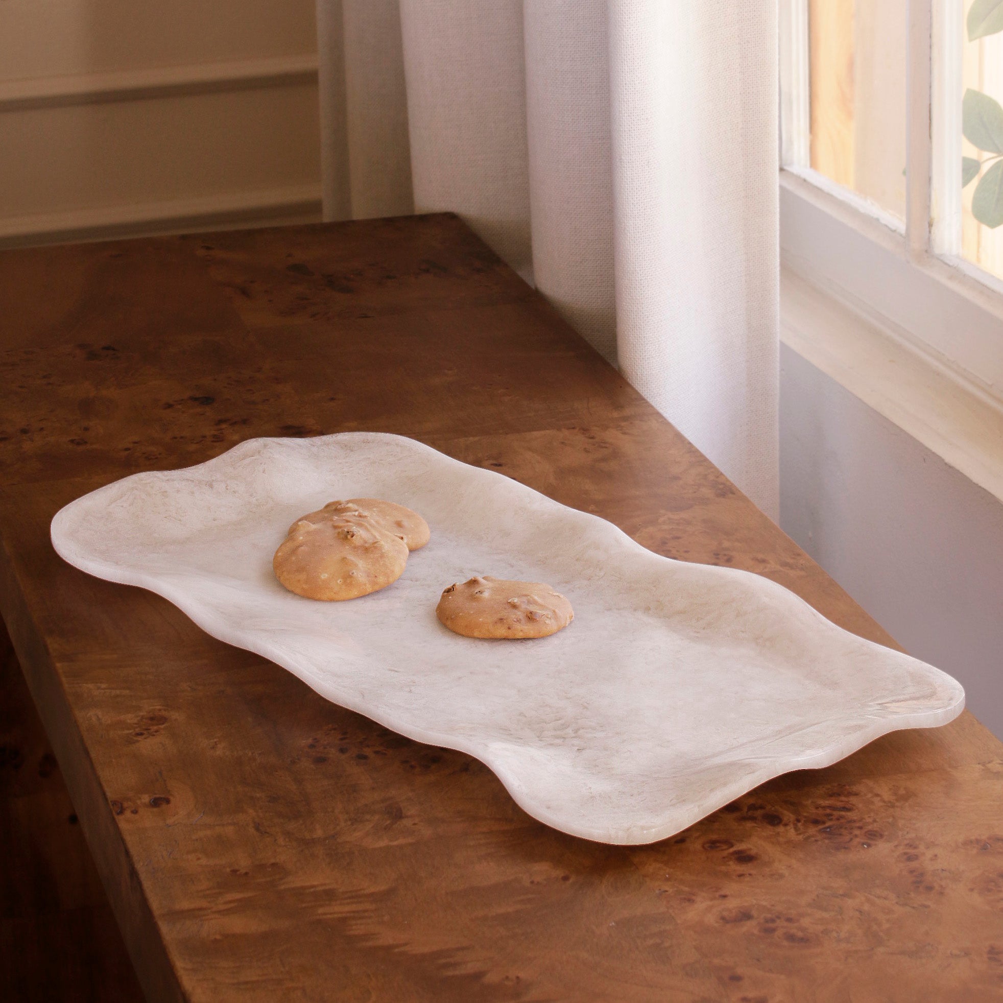 White alabaster resin tray with cookies on a wooden surface near a window