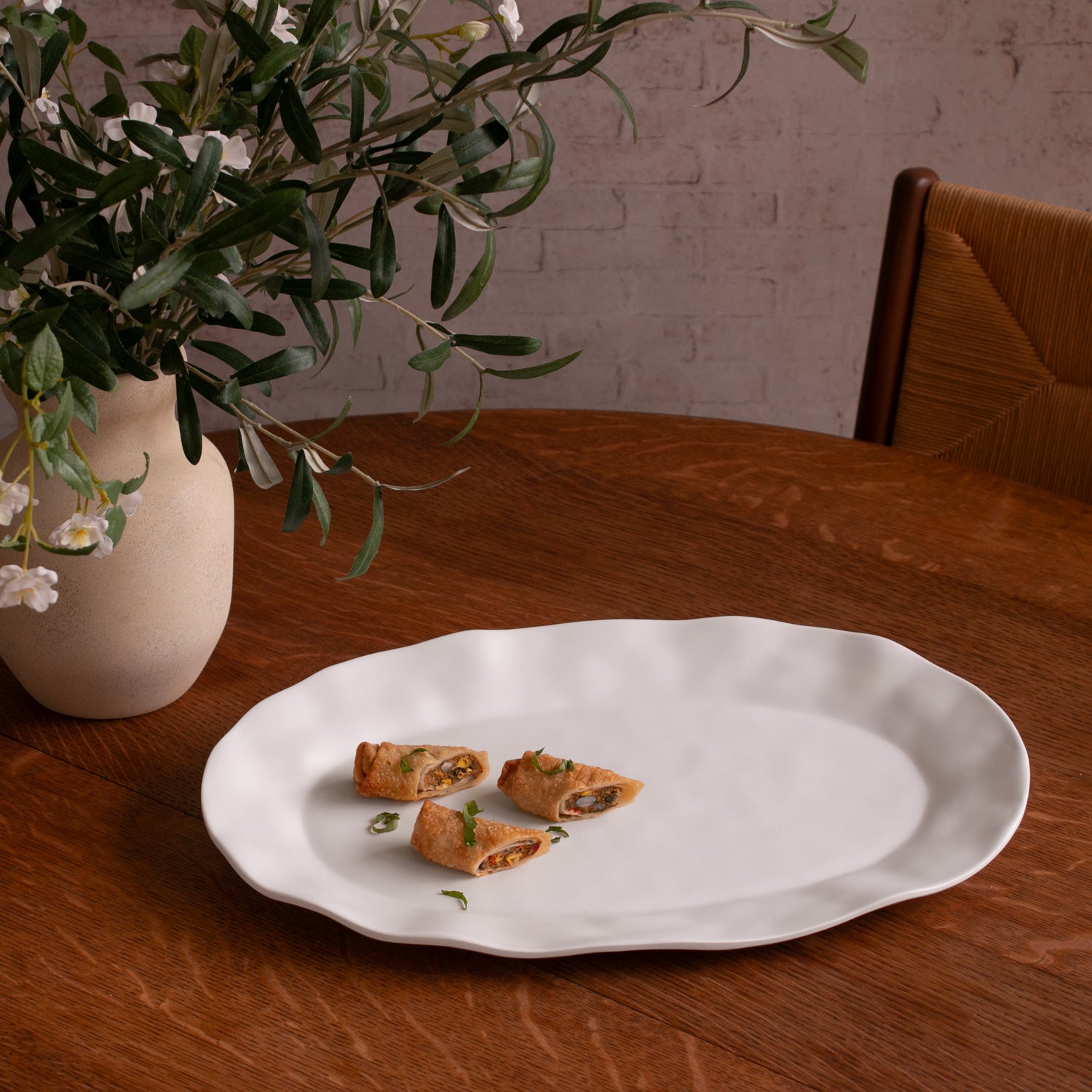 White tray with food on a wooden table next to a vase with greenery