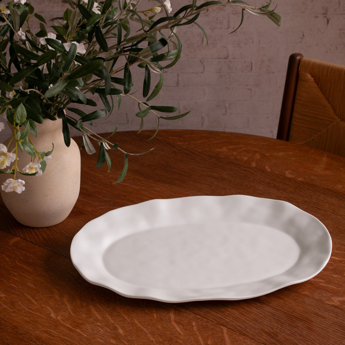 White oval tray on a wooden table with a vase of greenery in the background.