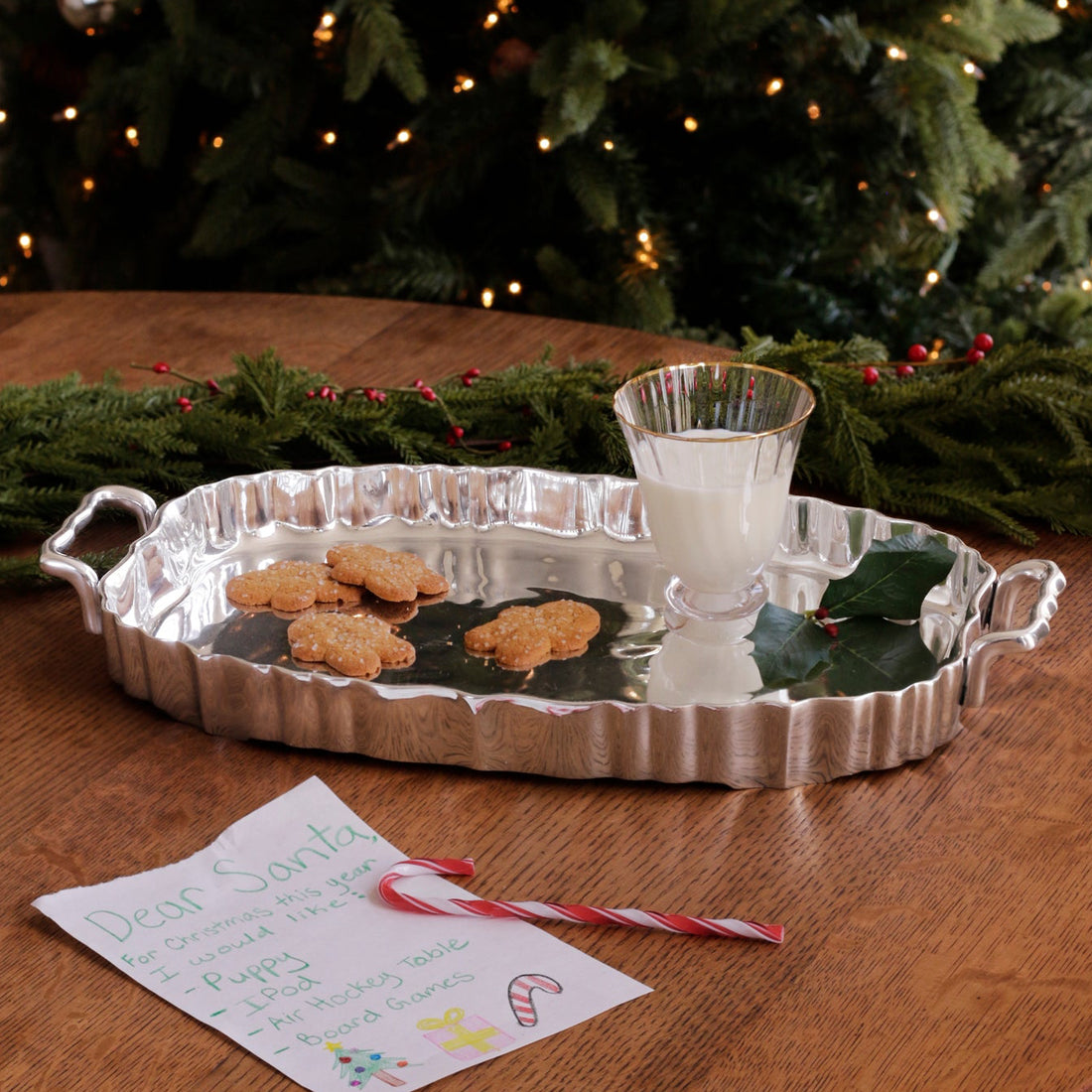 Silver tray with cookies, milk, and a candy cane in front of a Christmas tree.