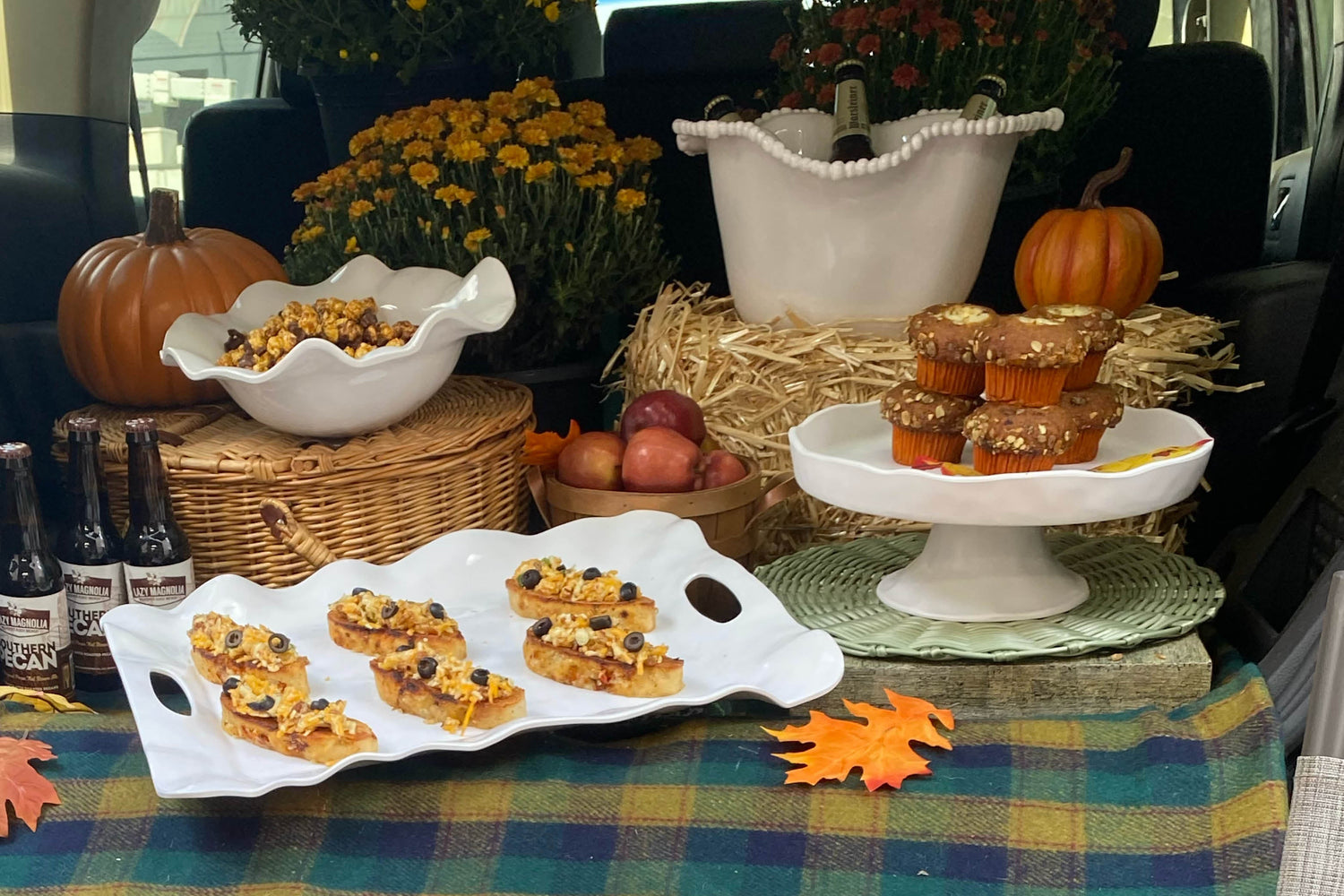 An elegant tailgating party with appetizers, an ice bucket with bottles of beer and fall floral arrangements