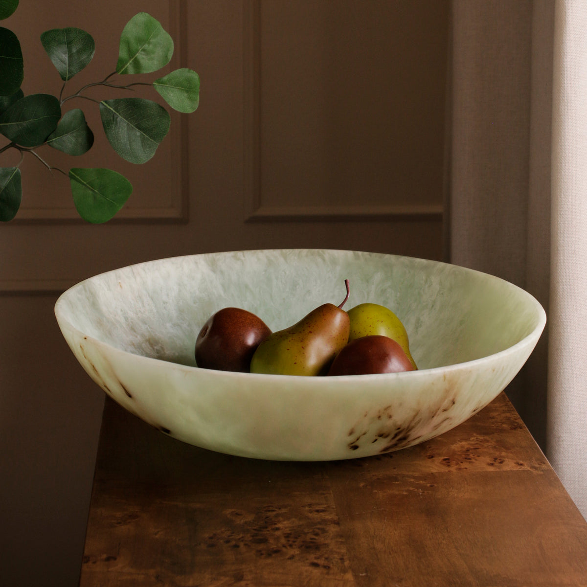 Decorative green resin bowl with fruits on a wooden surface