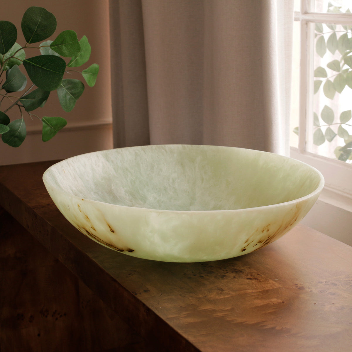 Green marble pattern resin 
bowl on a wooden surface with a window and plant in the background