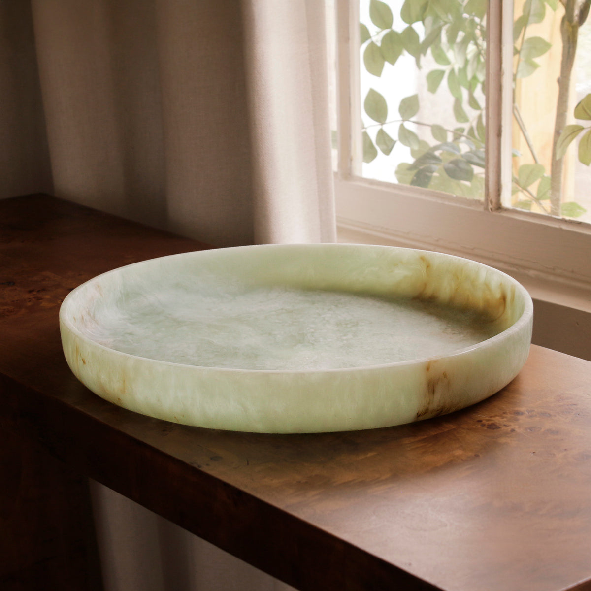 Green marble pattern resin tray on a wooden surface with a window in the background