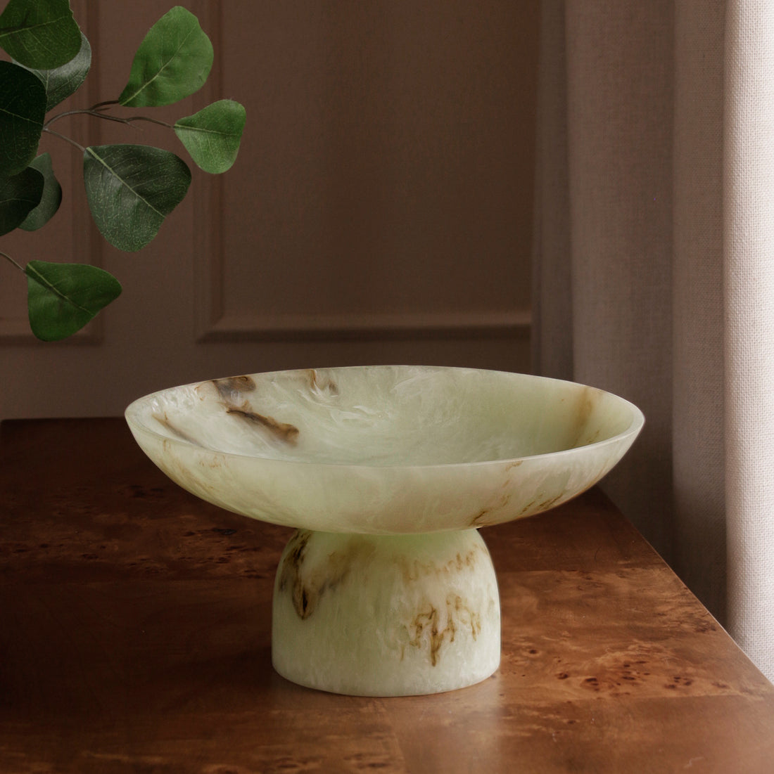 Jade swirl marble pattern resin pedestal bowl on a wooden surface with a neutral background