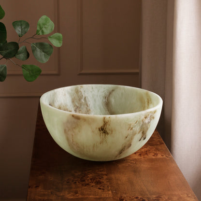Jade swirl marble pattern resin bowl on a wooden table with a plant in the background