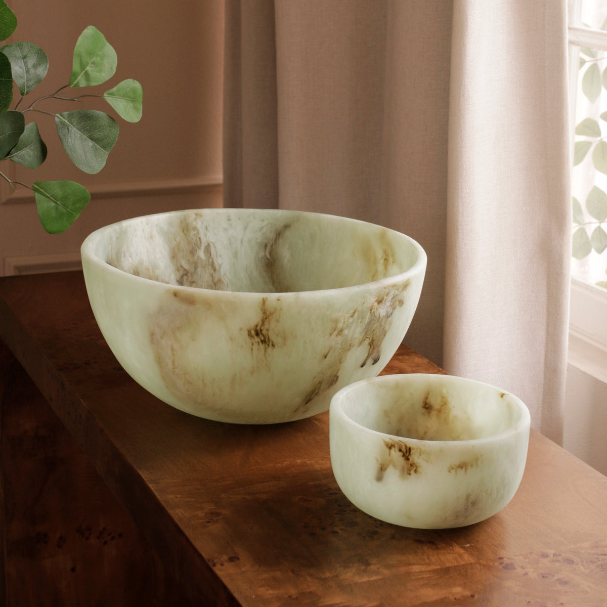 Two Jade swirl marble pattern resin bowls of different sizes on a wooden surface with a natural light background