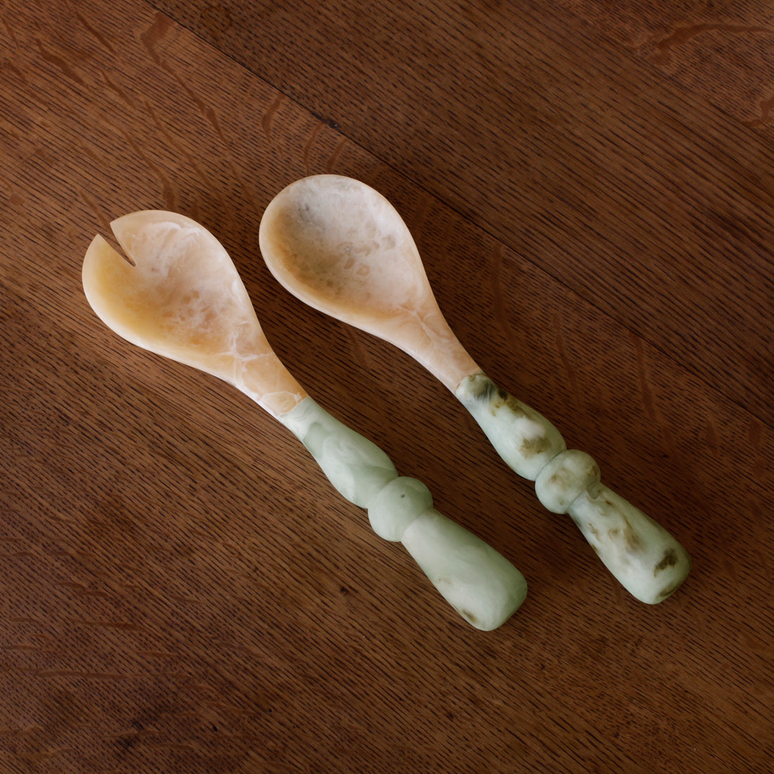 Two Salad Servers with jade swirl marble pattern resin handles on a wooden surface
