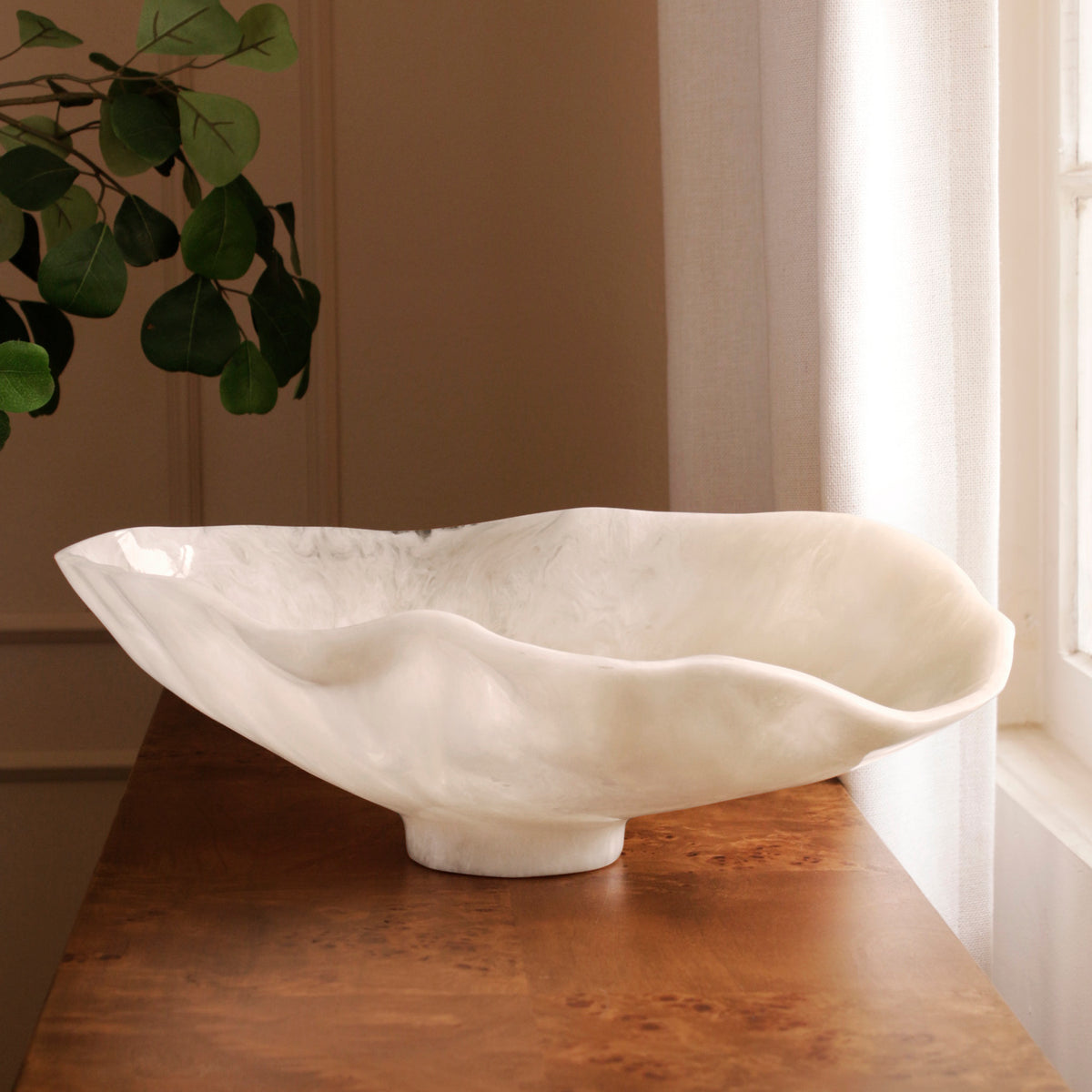 White resin bowl on a wooden surface with a plant in the background