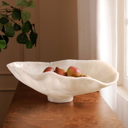 White resin bowl with fruits on a wooden table, plant in the corner