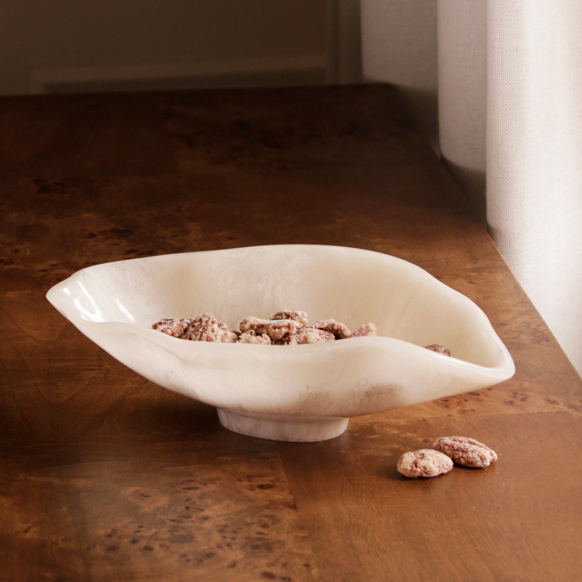 White resin bowl with scattered nuts on a wooden surface