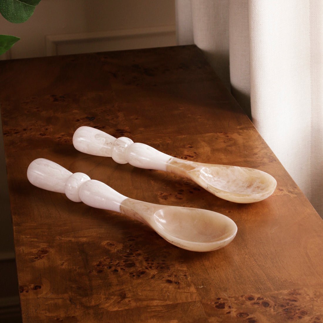 Two resin spoons with white handles on a wooden surface with a soft focus background