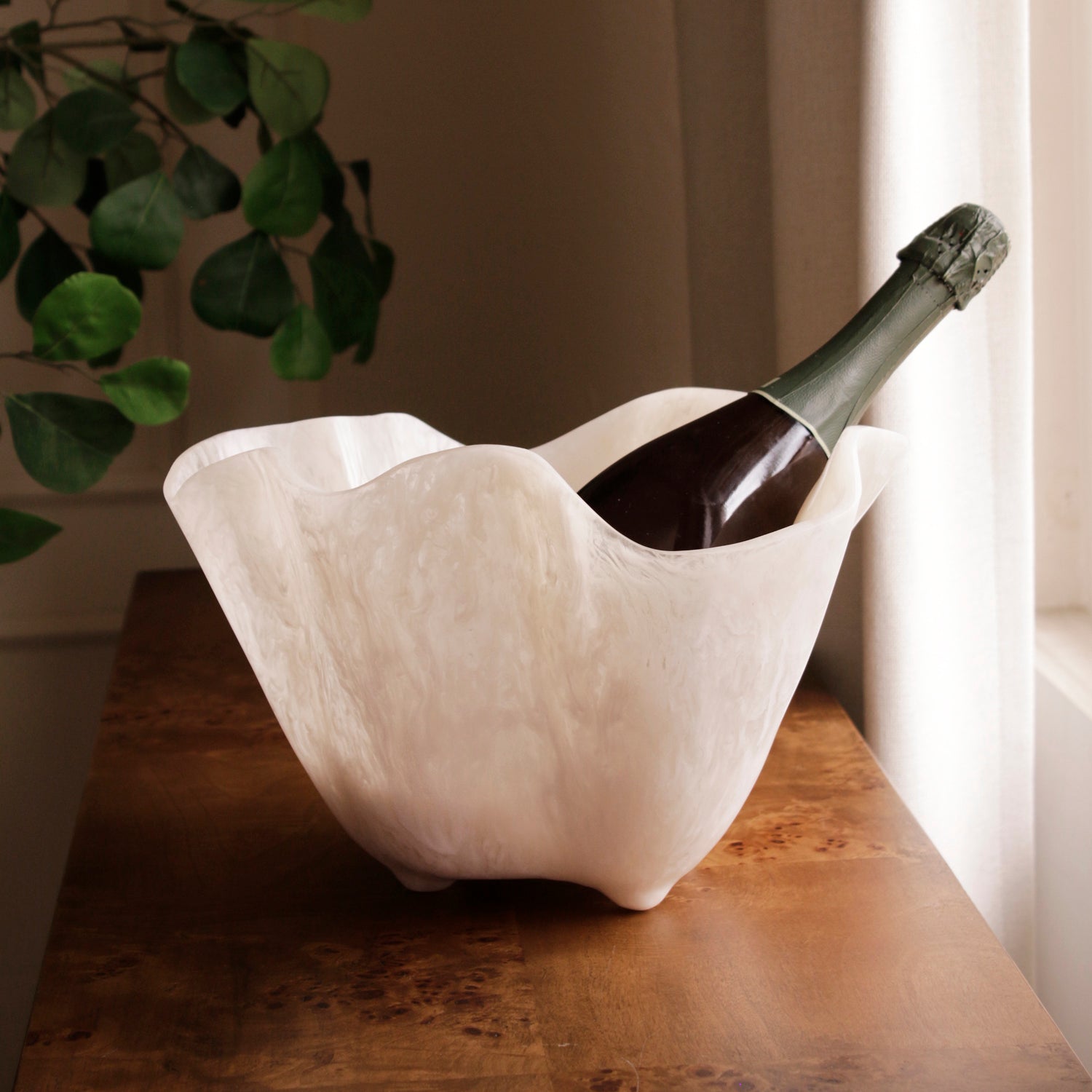 White resin ice bucket with a bottle of champagne on a wooden surface.