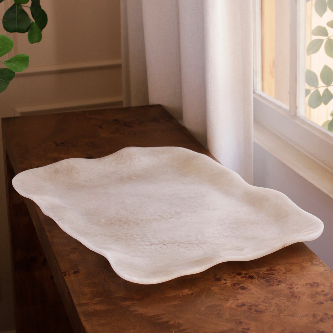 White alabaster resin tray on a wooden surface with a window and plant in the background