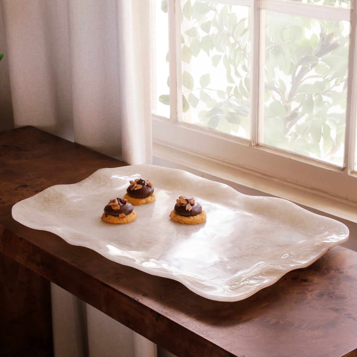 White alabaster resin tray with cookies on a wooden surface near a window