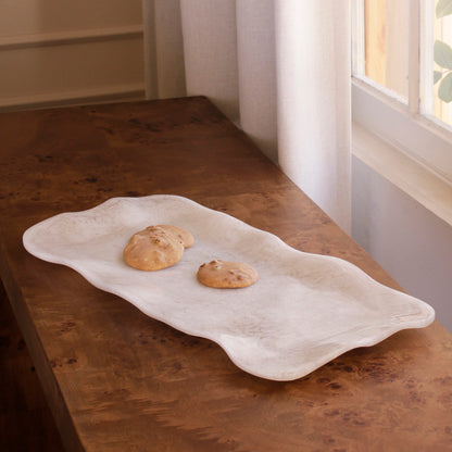 White alabaster resin tray with cookies on a wooden surface near a window