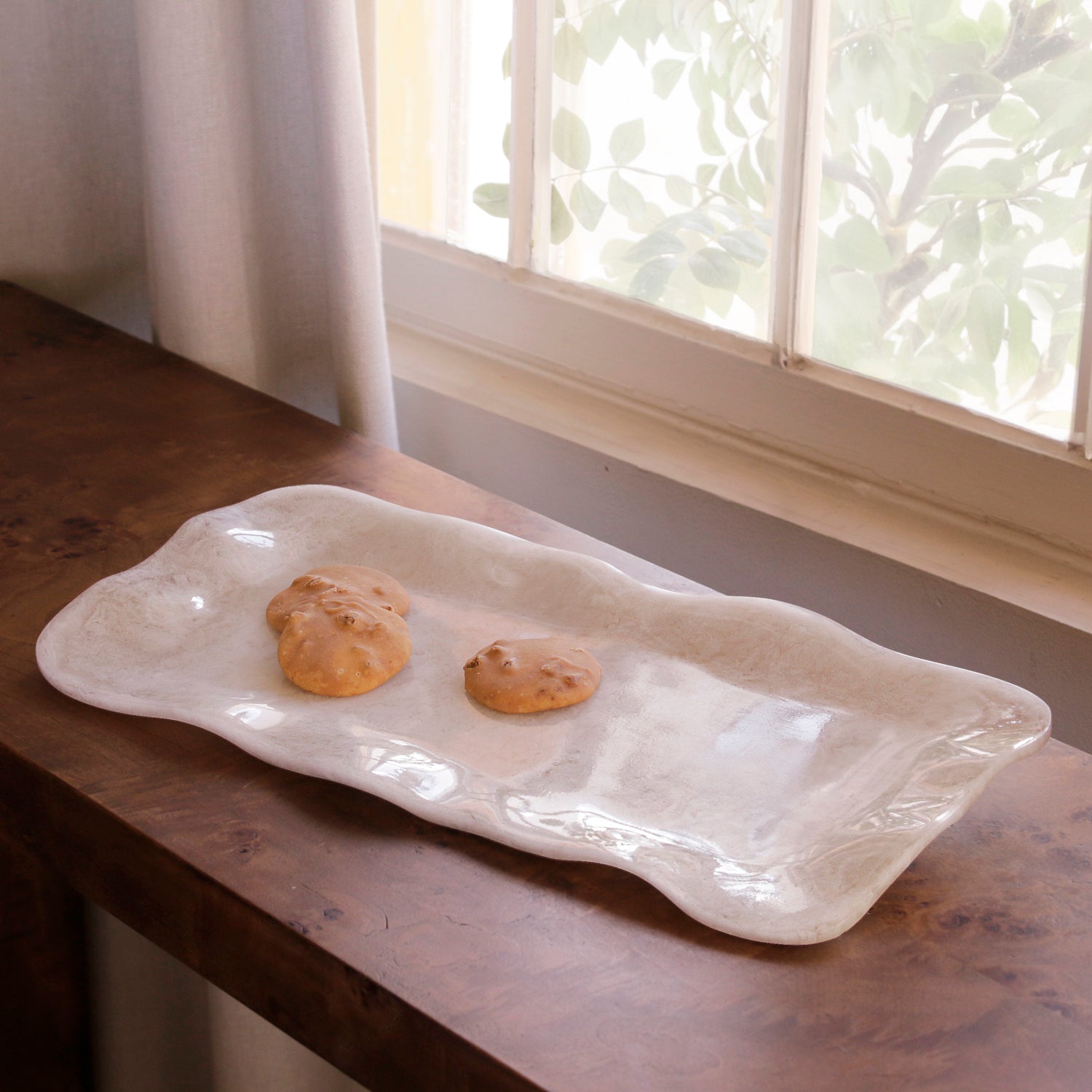 White alabaster resin tray with two cookies on a wooden surface near a window