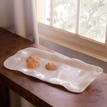 White alabaster resin tray with two cookies on a wooden surface near a window