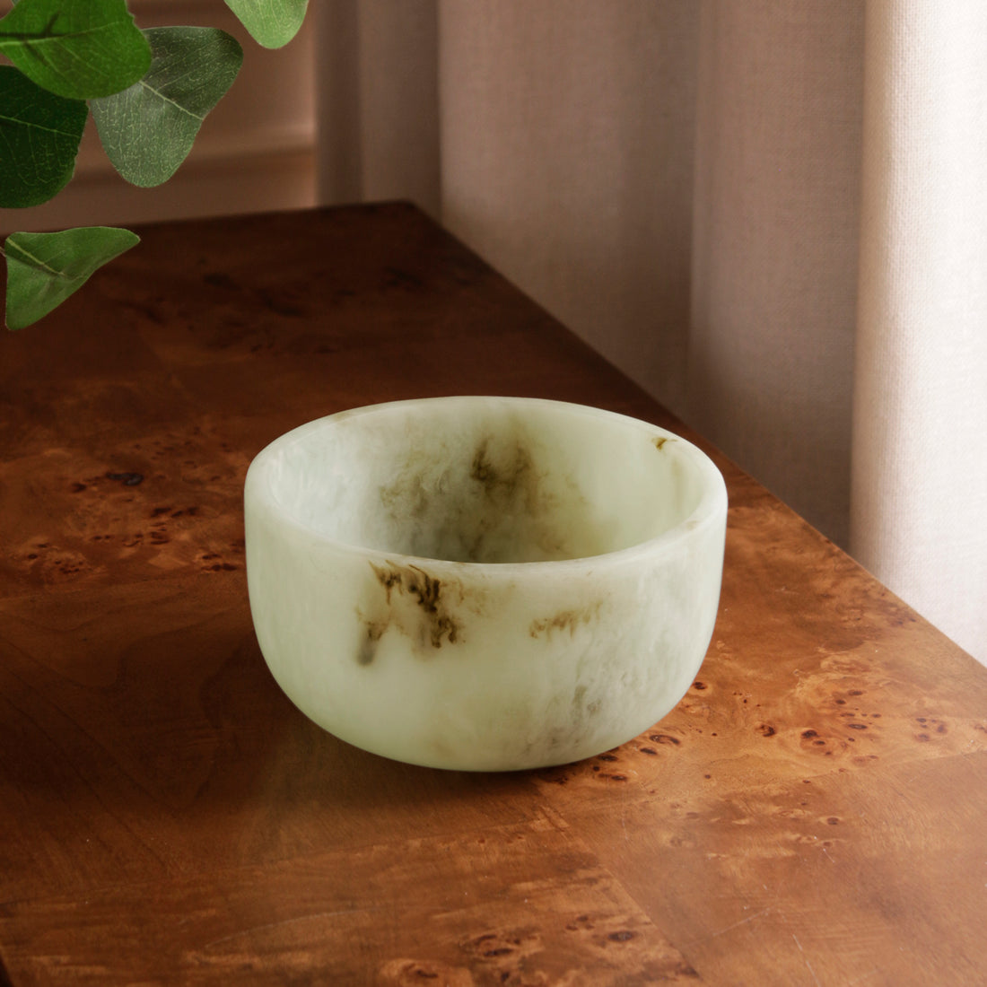 Jade swirl marble pattern resin bowl on a wooden surface with a plant in the corner
