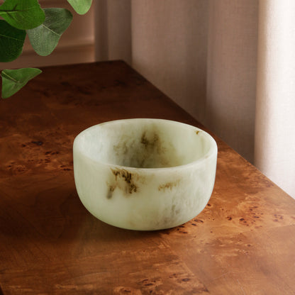 Jade swirl marble pattern resin bowl on a wooden surface with a plant in the corner