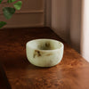 Jade swirl marble pattern resin bowl on a wooden surface with a plant in the corner