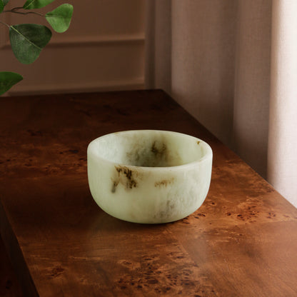 Jade swirl marble pattern resin bowl on a wooden surface with a plant in the corner
