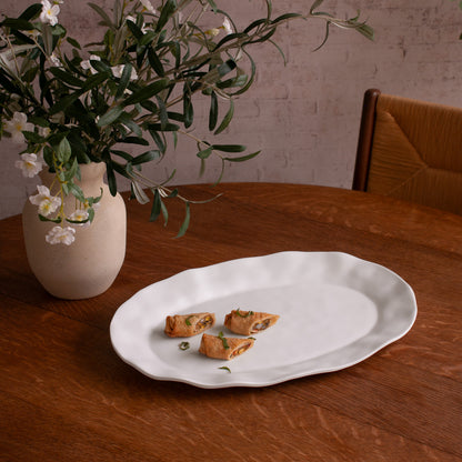 White tray with food on a wooden table next to a vase with flowers